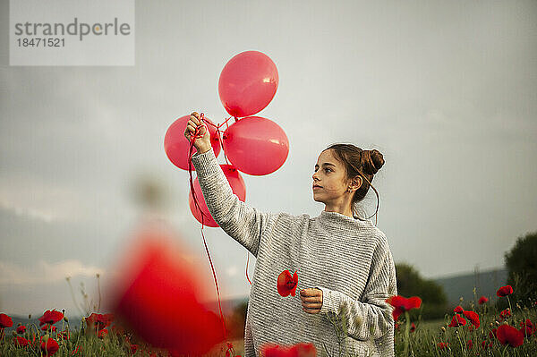 Nachdenkliches Mädchen mit Mohnblume  das rote Luftballons unter dem Himmel hält