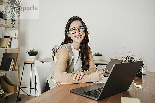 Glückliche Geschäftsfrau sitzt vor Laptop am Schreibtisch