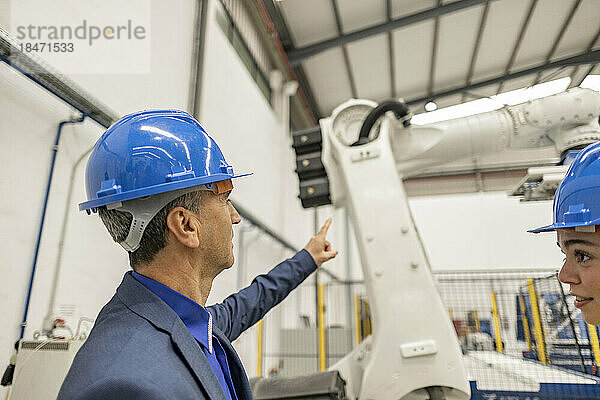 Reifer Geschäftsmann zeigt auf Roboterarm in der Fabrik