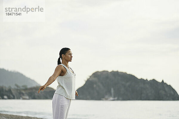 Frau praktiziert Yoga vor dem Meer