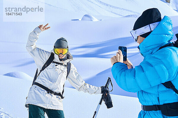 Reifer Mann fotografiert glückliche Frau mit Smartphone im Schnee