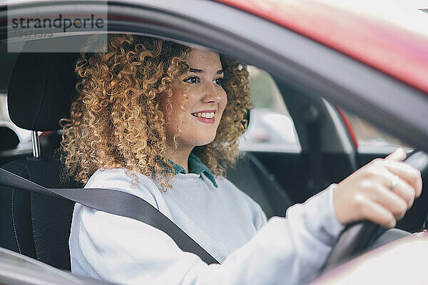 Smiling woman with curly hair driving car