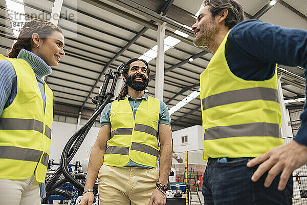 Glückliche Ingenieure in reflektierender Kleidung reden in der Fabrik miteinander