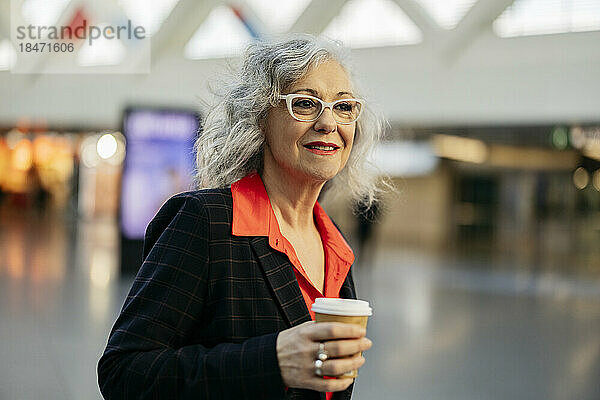 Reife Geschäftsfrau mit Brille und Einweg-Kaffeetasse an der U-Bahn-Station