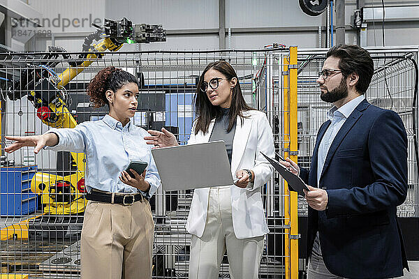 Geschäftsfrau hält Laptop in der Hand und diskutiert mit Kollegen in der Fabrik