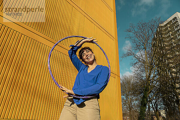 Glückliche Frau mit Hula-Hoop-Reifen in der Nähe eines gelben Frachtcontainers