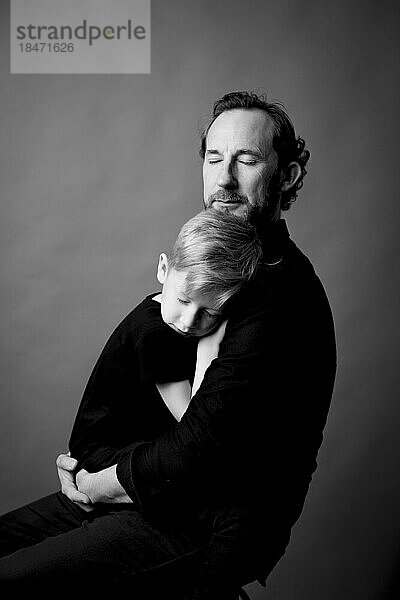 Zärtlicher Vater mit geschlossenen Augen umarmt seinen Sohn
