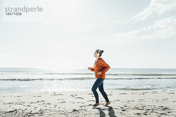 Reife Frau mit Kopfhörern joggt am Strand