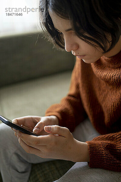 Teenager sitzt zu Hause auf dem Sofa und nutzt sein Smartphone