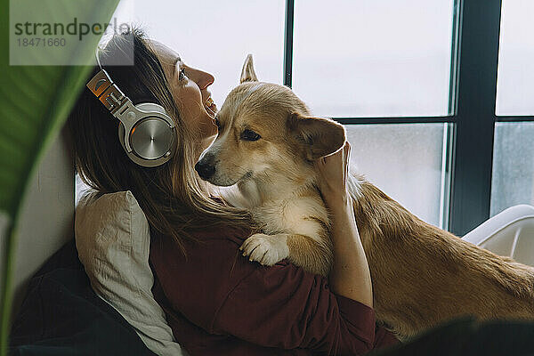 Lächelnde Frau  die zu Hause mit ihrem Hund Musik über Kopfhörer hört