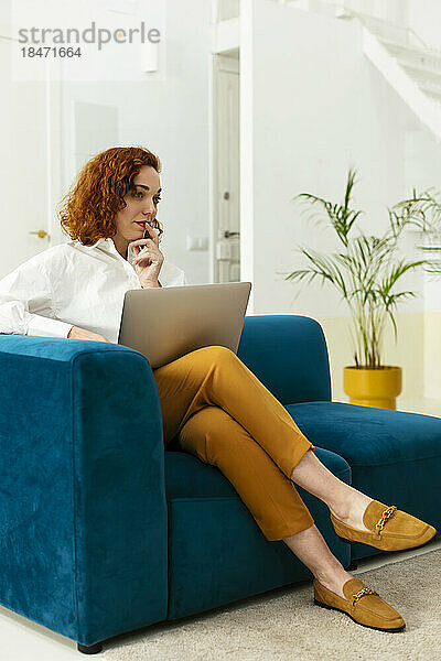 Nachdenkliche Geschäftsfrau sitzt mit Laptop auf dem Sofa im Büro