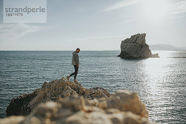 Mann geht auf Felsen vor dem Meer