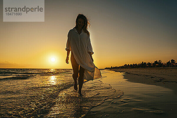 Unbekümmerte Frau spaziert bei Sonnenaufgang am Strand entlang