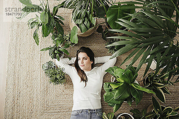 Nachdenkliche Frau entspannt sich zu Hause neben Pflanzen auf dem Teppich