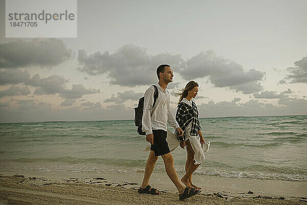 Junges Paar geht gemeinsam am Strand in Ufernähe spazieren