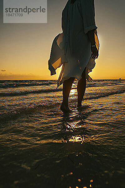 Frau spaziert bei Sonnenaufgang im Meer am Strand