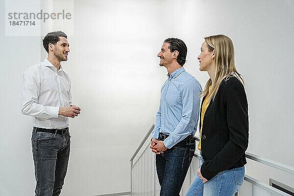Smiling businessman talking to colleagues standing near railing at office