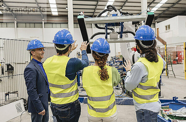 Ingenieure mit Schutzhelm untersuchen Maschinenteile in einer Robotikfabrik