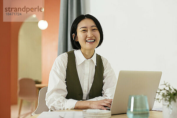 Glückliche Geschäftsfrau sitzt am Schreibtisch mit Laptop im Büro