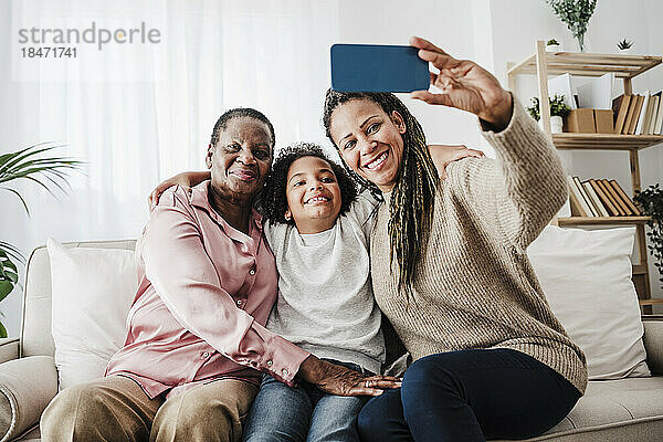 Frau macht Selfie mit Familie  die zu Hause auf dem Sofa sitzt