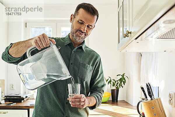 Mann gießt Wasser aus einer Filterkanne in ein Glas in der Küche