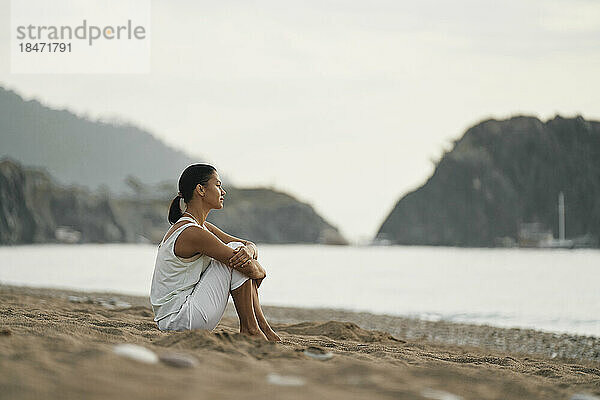 Nachdenkliche Frau sitzt auf Sand am Strand