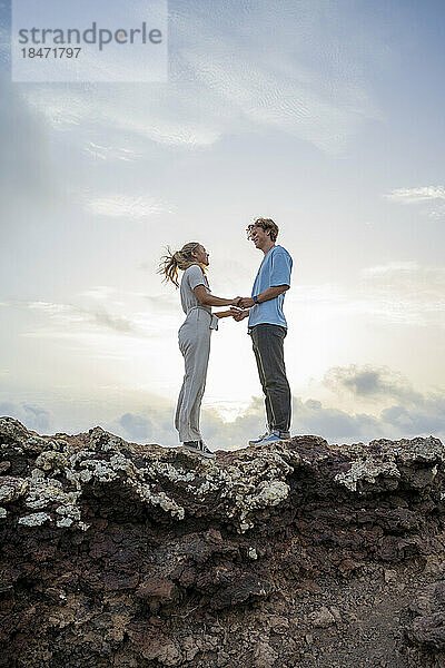 Junges Paar steht auf einer Klippe und hält sich an den Händen