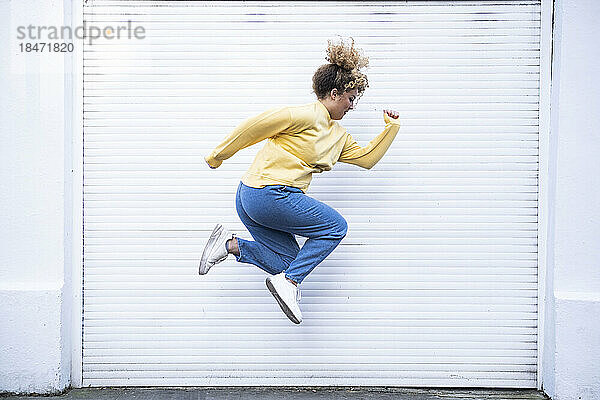 Carefree young woman jumping by white shutter