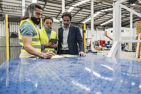 Geschäftsmann mit Ingenieuren  die in der Fabrik Notizen schreiben