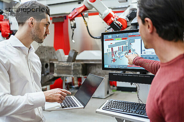 Ingenieur erklärt Kollegen mit Laptop in Roboterfabrik