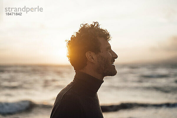 Von hinten beleuchteter Mann vor dem Meer bei Sonnenuntergang
