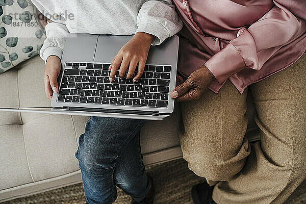 Mädchen benutzt Laptop und Großmutter sitzt zu Hause auf dem Sofa