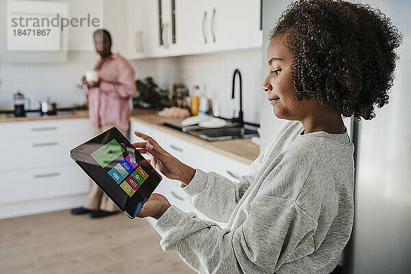 Mädchen mit lockigem Haar benutzt Tablet-PC in der heimischen Küche