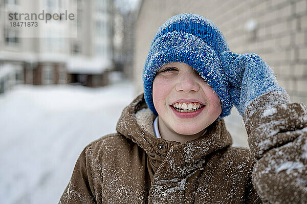 Fröhlicher Junge mit blauer Strickmütze im Schnee