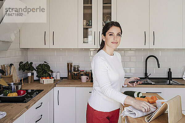 Lächelnde Frau mit Tablet-PC und Smartphone in der heimischen Küche