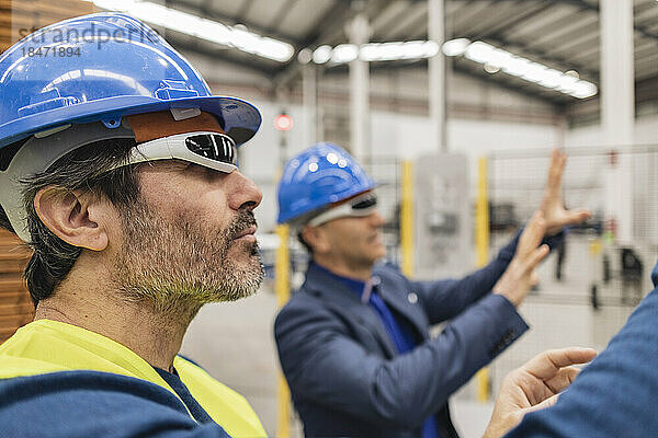 Reifer Ingenieur mit intelligenter Brille steht seinem Kollegen in der Fabrik zur Seite