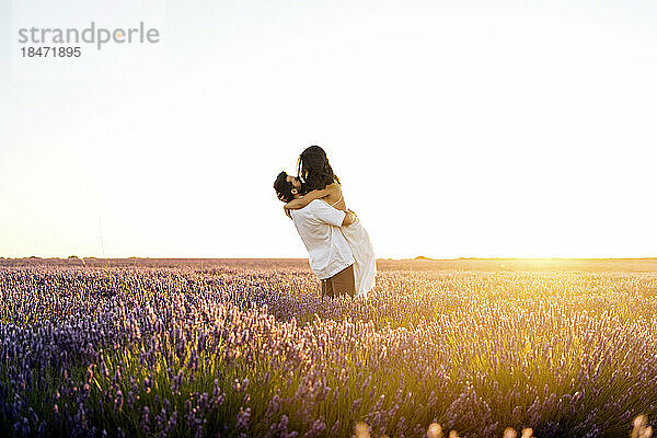 Man carrying woman in lavender field at sunset