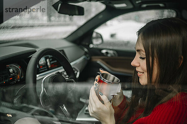 Lächelnde Frau  die im Auto Kaffee trinkt