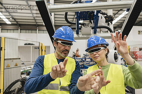 Reifer Ingenieur mit Kollegen  der eine intelligente Brille in der Robotikfabrik trägt