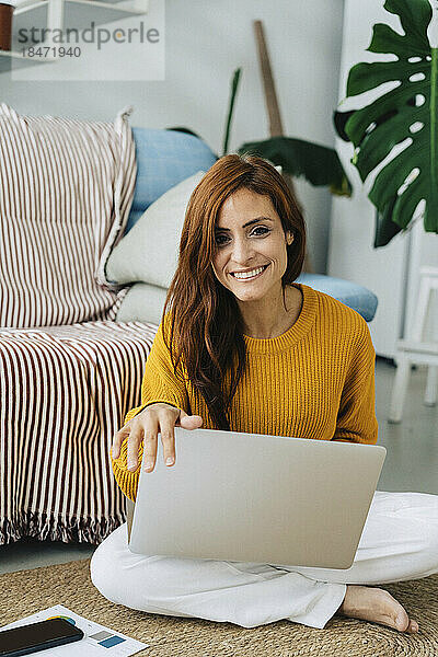Glückliche Frau mit Laptop sitzt zu Hause im Wohnzimmer