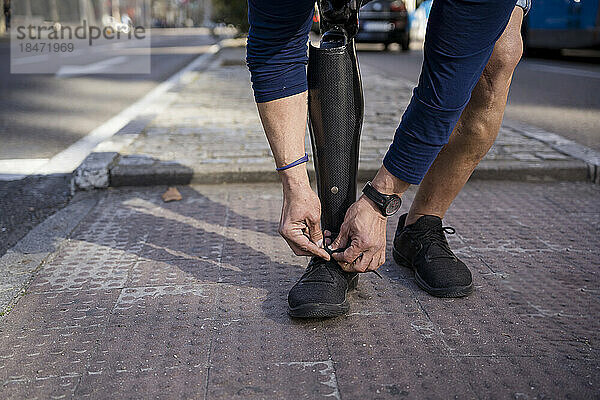 Mann mit amputiertem Bein bindet Schnürsenkel auf Fußweg