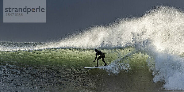 Abenteuerlustiger Mann balanciert bei Sonnenuntergang mit Surfbrett auf Wellen