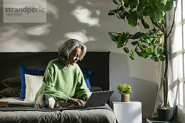 Frau benutzt Laptop auf dem Bett im Schlafzimmer zu Hause