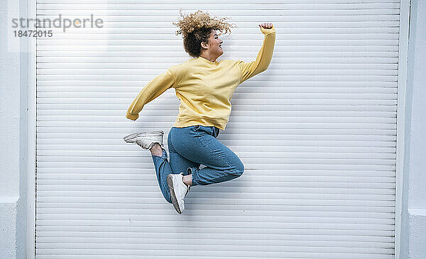 Carefree young woman jumping by closed white shutter