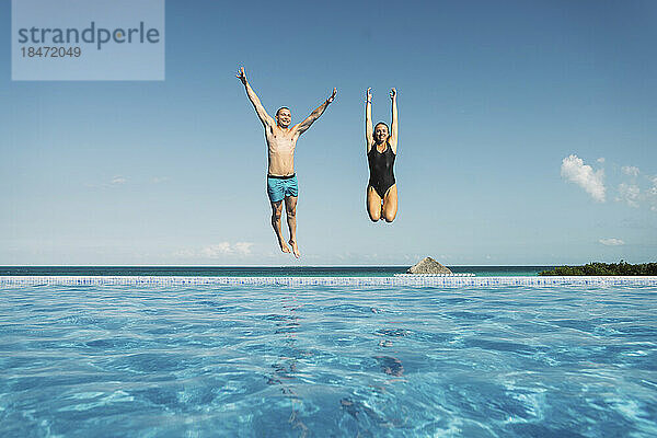 Sorgloses Paar springt mit erhobenen Armen im Schwimmbad