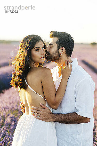 Mann küsst Frau auf die Wange  die im Lavendelfeld steht