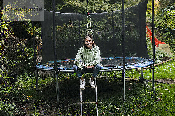 Glückliche Frau sitzt auf Trampolin im Garten