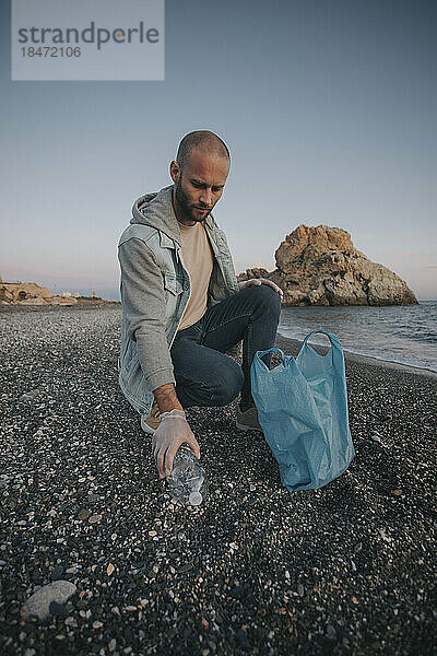 Mann reinigt bei Sonnenuntergang Müll vom Strand