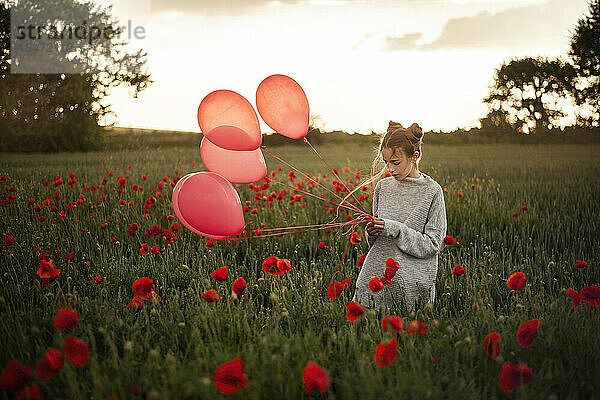 Mädchen mit roten Luftballons steht im Mohnfeld