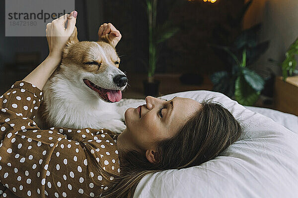 Lächelnde Frau  die zu Hause im Bett liegt und mit Hundeohren spielt